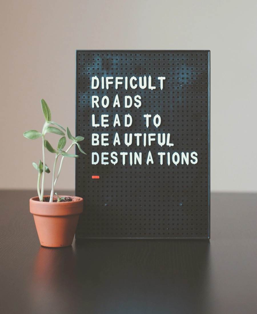 Letter board reading &lsquo;Difficult roads lead to beautiful destinations&rsquo; beside a potted seedling
